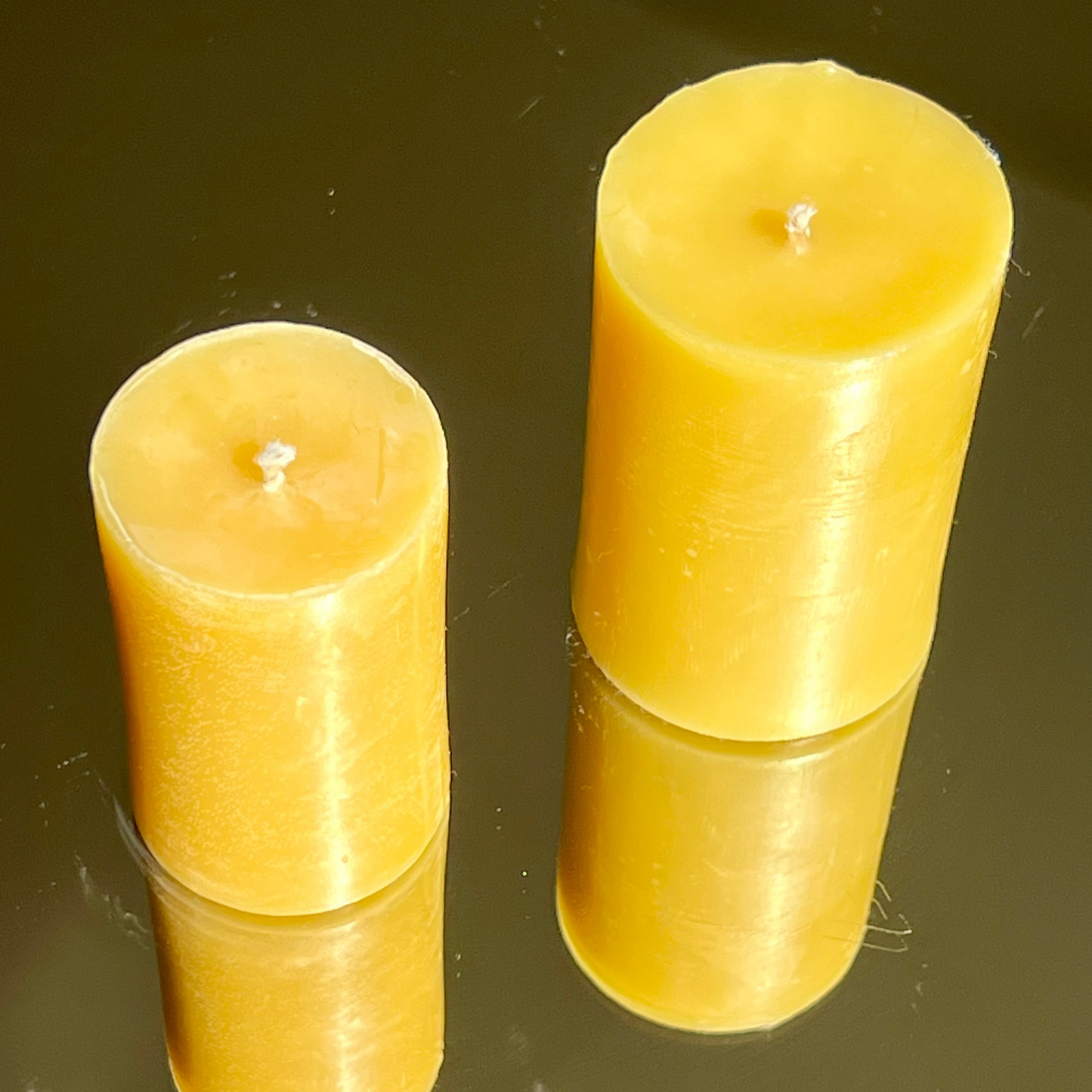 Two yellow candles on a reflective black surface