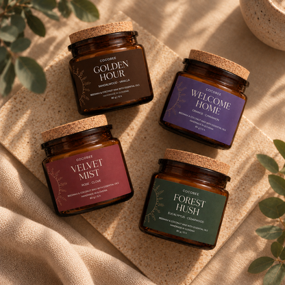 Quattro candele CocoBee Sunset Ritual in vetro ambrato con coperchi in sughero, su lino beige: Golden Hour, Welcome Home, Velvet Mist e Forest Hush.