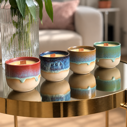 Four ceramic candles with colorful glazed drips in red, blue, tan, and green, arranged on a round gold table in a softly lit living room setting.