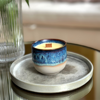 Ceramic wood wick candle with blue glaze on a gray plate with a blurred background