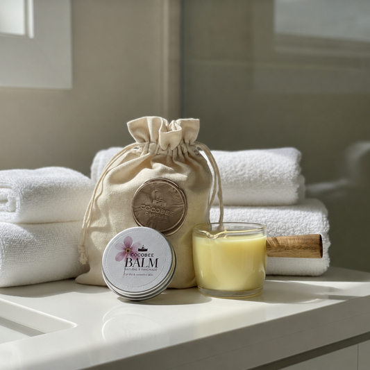 Bath products including towels, a bag, a jar of balm, and a candle on a marble surface.