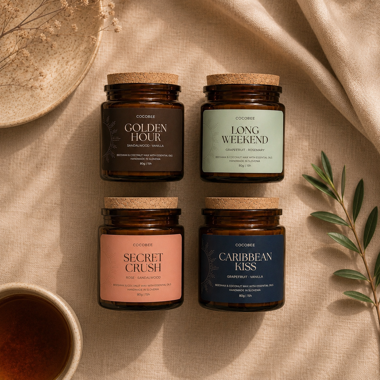Four candles with different scents on a textured surface with a cup and leaves.