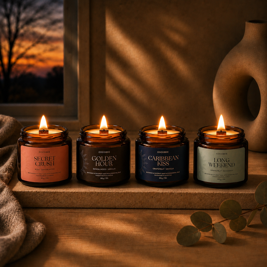 Four lit candles in labeled jars on a wooden surface with a warm, sunset-like background.