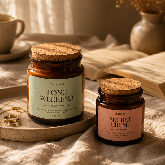 Two candles labeled 'Long Weekend' and 'Secret Crush' on a textured surface with a cup and book in the background.