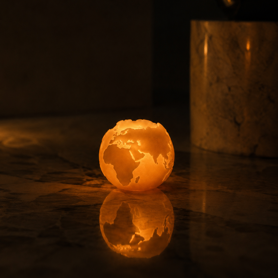 Globe-shaped beeswax candle on a reflective surface with a dark background